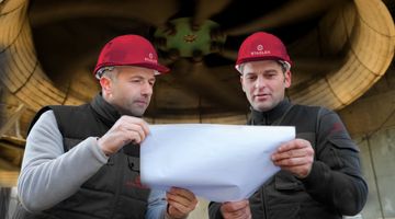Zwei Männer besprechen eine Technische Zeichnung vor einer Turbine