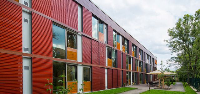 Seniorenheim mit Faserverbundplattenfassade Kempten Eine rote Fassade hinter einer grünen Wiese und einem Weg