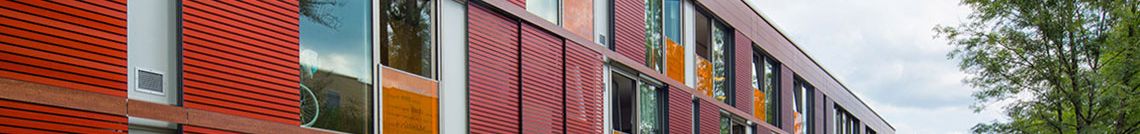 Eine rote Fassade hinter einer grünen Wiese und einem Weg