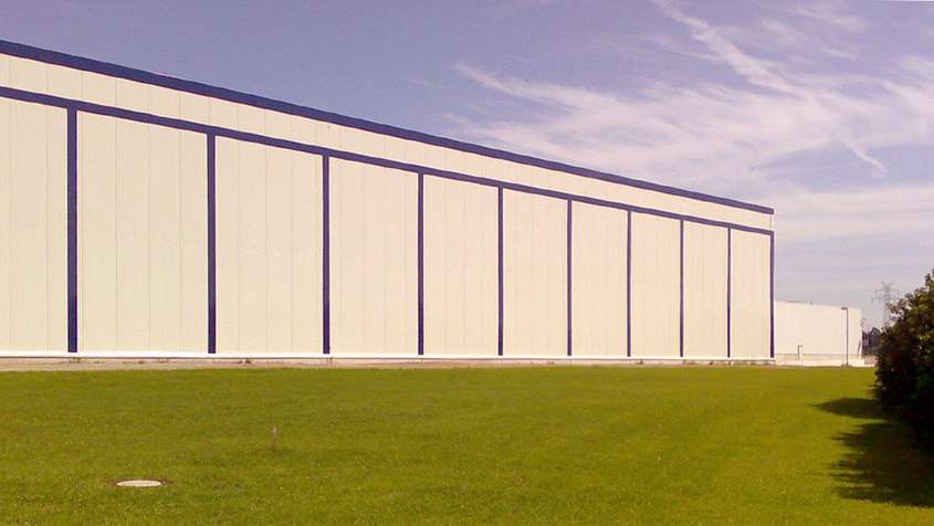 NULL GRAD LAGER EDEWECHT Gemähte Rasenfläche mit einer weißen Wand mit blauen Streifen im Hintergrund