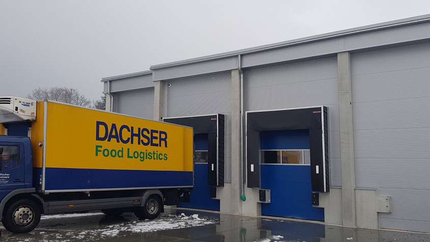 VERLADEBRÜCKE MIT TORABDICHTUNG UND SEKTIONALTOR BODNEGG Verladebrücke an einem Lager mit einem blau-gelben LKW mit der Aufschrift „Dachser Food Logistics“