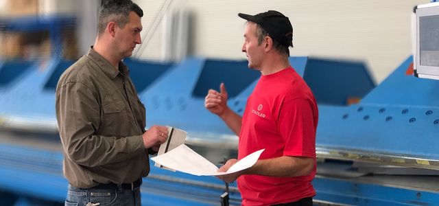 Two men talking in front of a machine