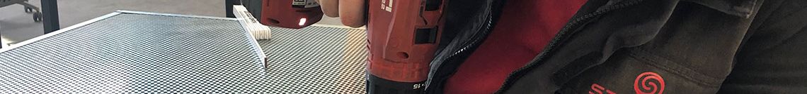 Ein Mann, der mit einem Akkuschrauber ein Lochblech in einem Rahmen fixiert