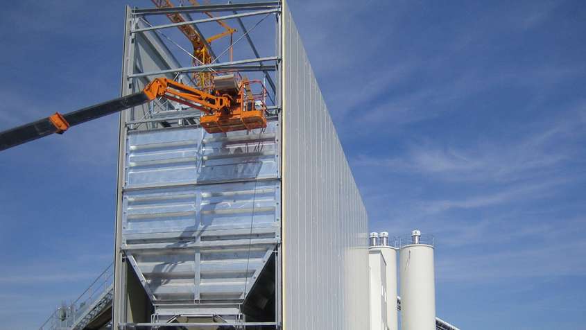 SILOVERKLEIDUNG Orangener Kran vor einem unfertigen Bauteil