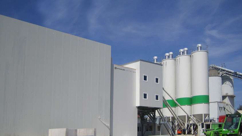 Three silos with a green stripe behind a large building composed of multiple rectangualr boxes