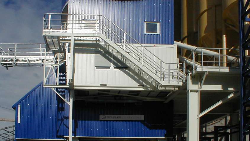 MASCHINENVERKLEIDUNG LÖTSCHBERGTUNNEL Weiße Treppe an der Seite eines blauen Metallgebäudes